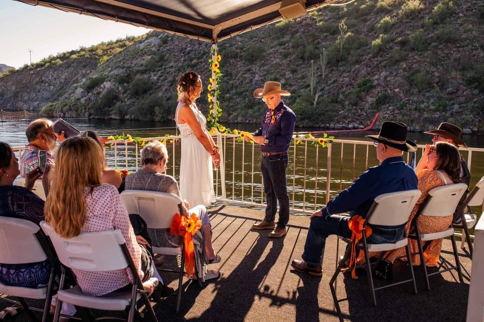 A beautiful outdoor wedding ceremony taking place on a riverbank, featuring a couple exchanging vows with family and friends in a picturesque setting.