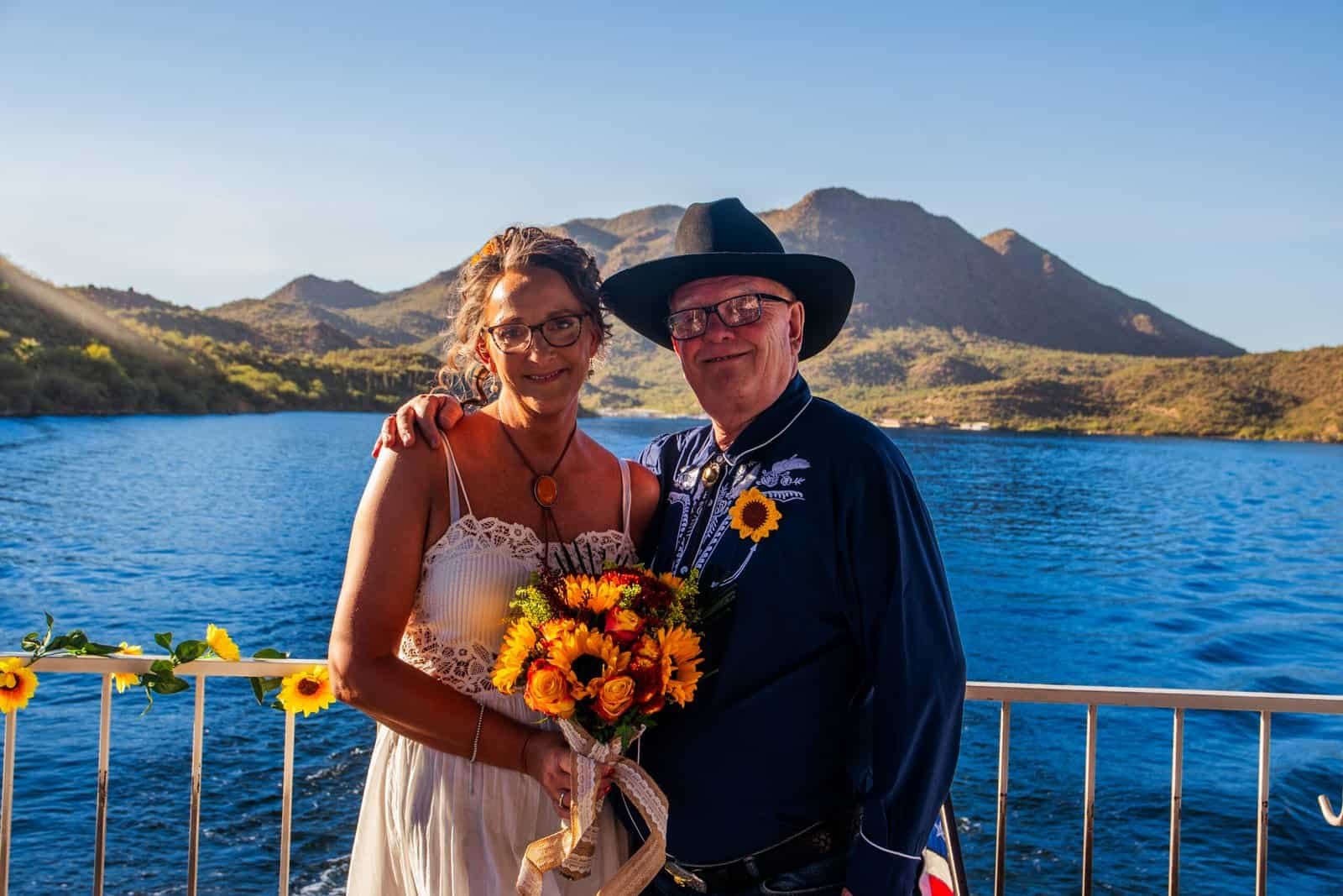 A joyful wedding scene featuring a couple holding a bouquet near a scenic lake with mountains in the background.