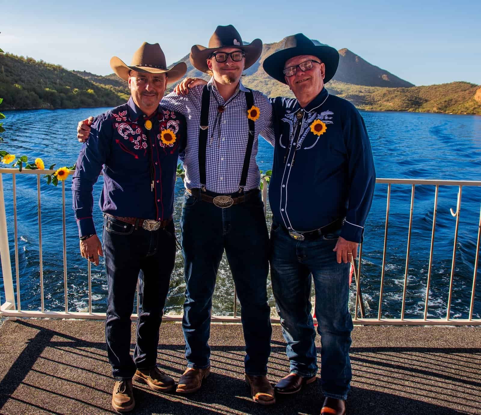 Three friends dressed in Western attire enjoying a scenic boat ride on a lake surrounded by mountains.