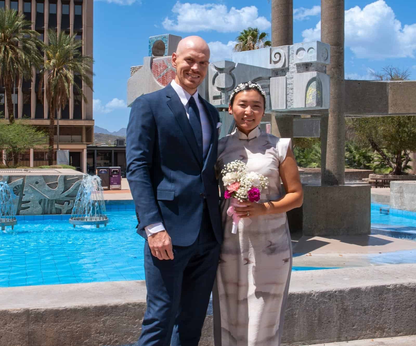 Happy wedding couple posing outdoors with fountain and sculpture at Special Moment Video.