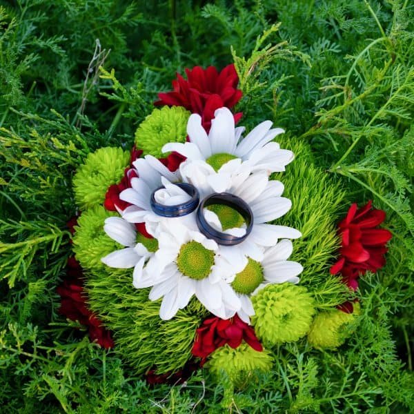 Beautiful wedding floral arrangement with rings, daisies, and lush greenery.