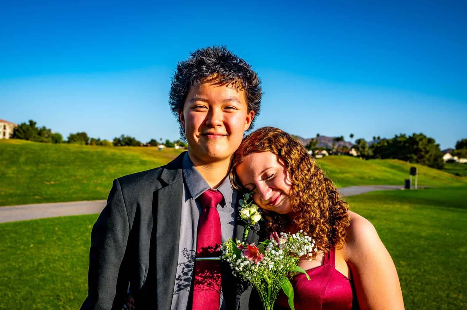 A joyful young couple dressed in formal attire celebrating prom night outdoors on a sunny day.