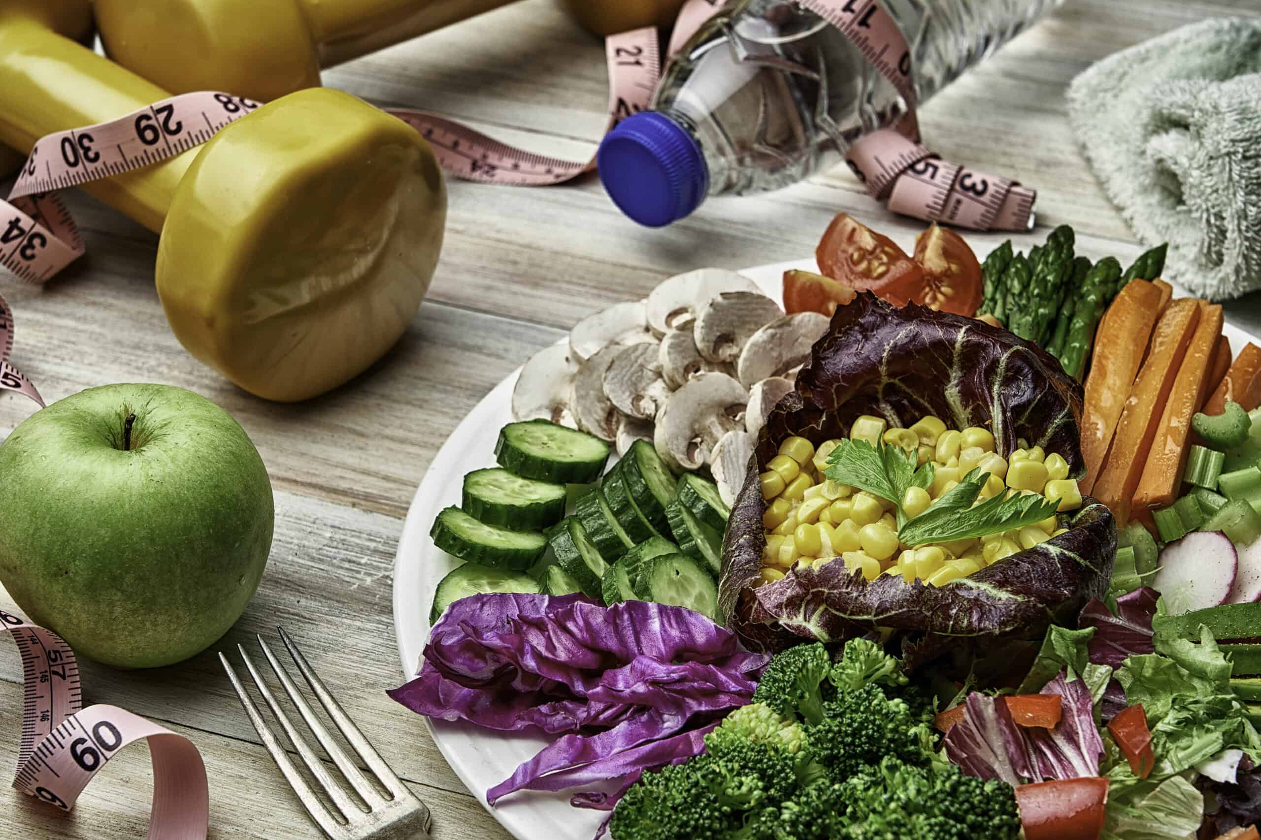Top view of a colorful spring salad on rustic white wood table. Included ingredients tomatoes, broccoli, lettuce, bell peppers, mushroom, carrots, radicchio, almonds.