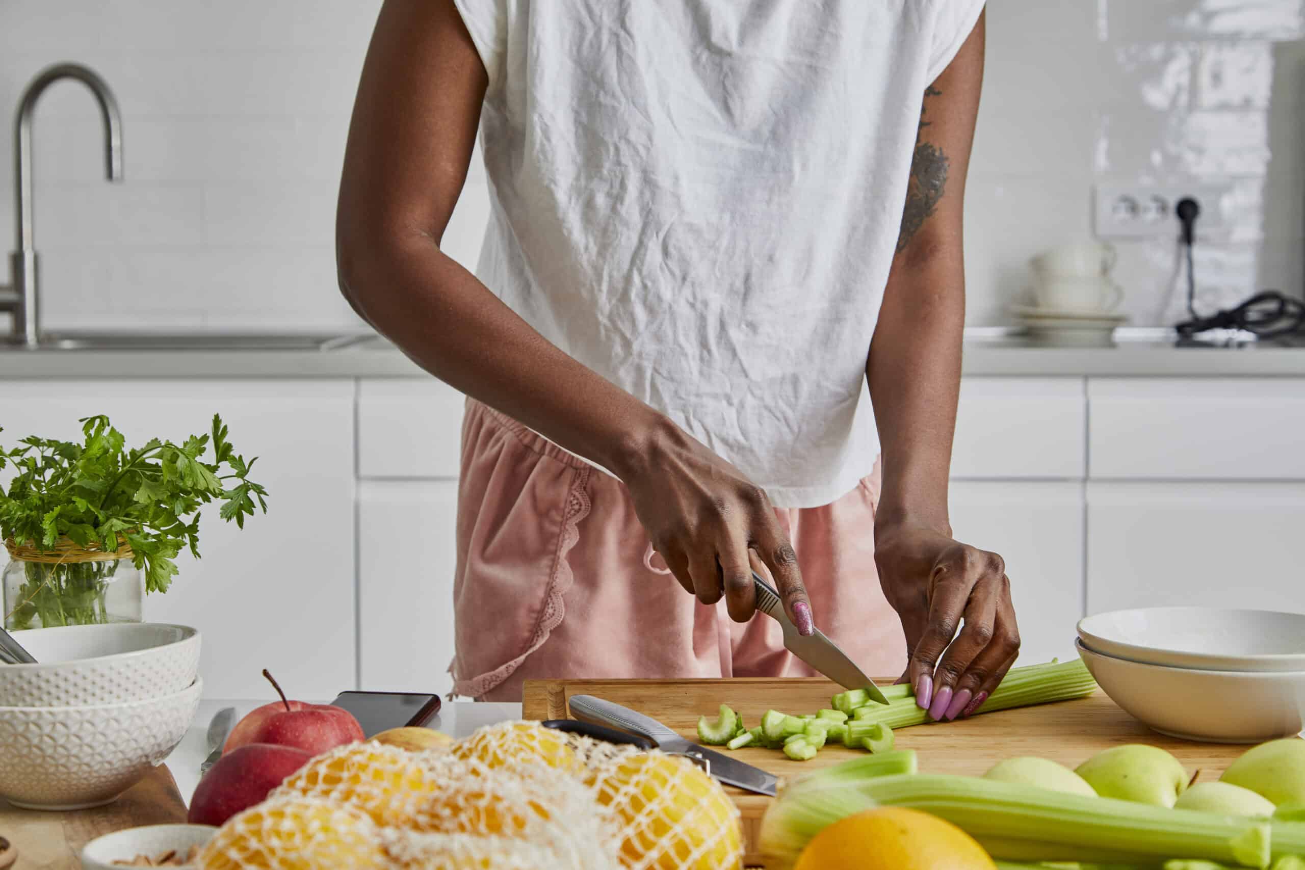 A young black adult woman in the kitchen, slicing a celery root on the table, fresh vegan or vegetarian food preparation at the kitchen table, representing healthy lifestyle, an image with a large copy space