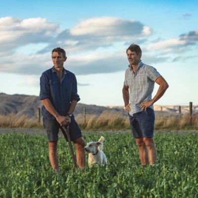 Brothers Andrew and James in farm field with dog looking out across farmland with hills in background