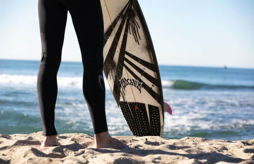 What Do You Wear Under a Wetsuit? 3 surfer wearing a wetsuit looking out to sea whilst holding his surf board