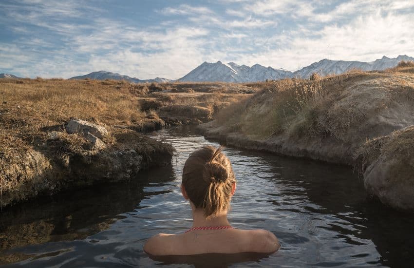 9 Benefits of Cold Water Swimming to Improve Your Health 1 The Benefits of Cold Water Swimming - Woman relaxing in cold water stream with a view of the mountains