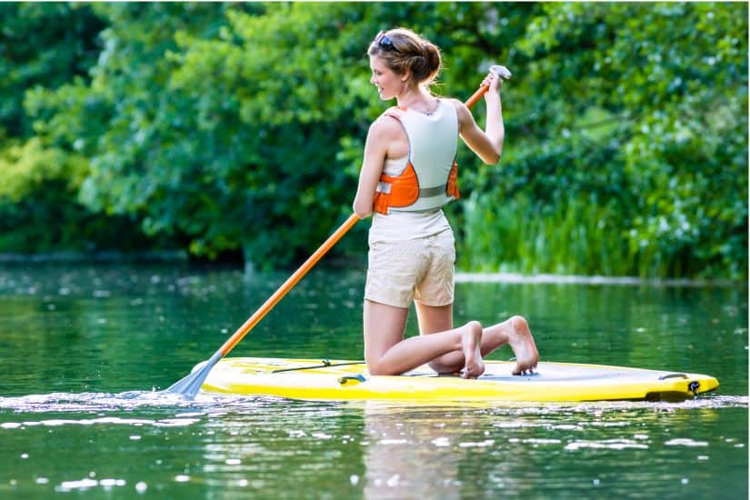 11 Best Life Jackets for Paddle Boarding (SUP) in 2025 14 Woman wearing a PFD kneeling on a SUP