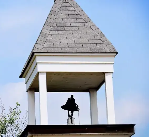 Bell tower with a shingled roof and a bell inside against a blue sky.