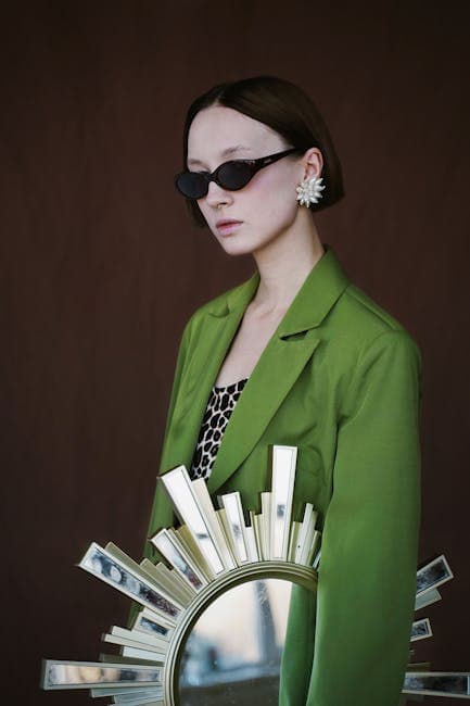 Moderne kvinde iført solbriller og grøn blazer, der holder en bog foran en spejlrefleks.