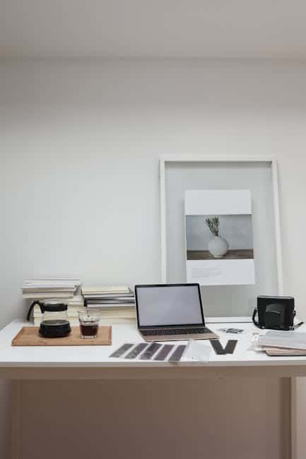 Moderne arbejdsstation med laptop, kamera og bøger i minimalistisk hjemmekontor.