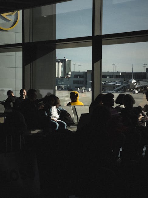 Passagerer venter i lufthavn med store vinduer og fly på rullebanen.