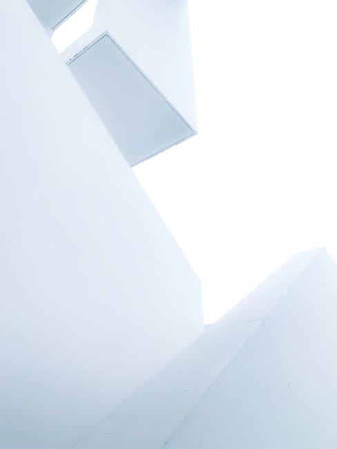 Minimalistisk hvid væg med loftsventilator og vindue.