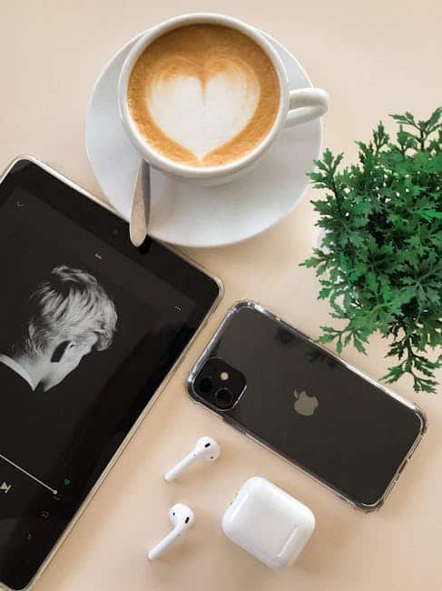 Kaffekop med lattekunst, smartphone, tablet og trådløse øretelefoner på bordet.