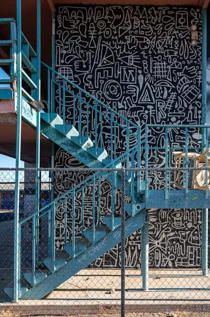 Udendørs blå metaltrappe foran væg med abstrakt grafisk kunst.