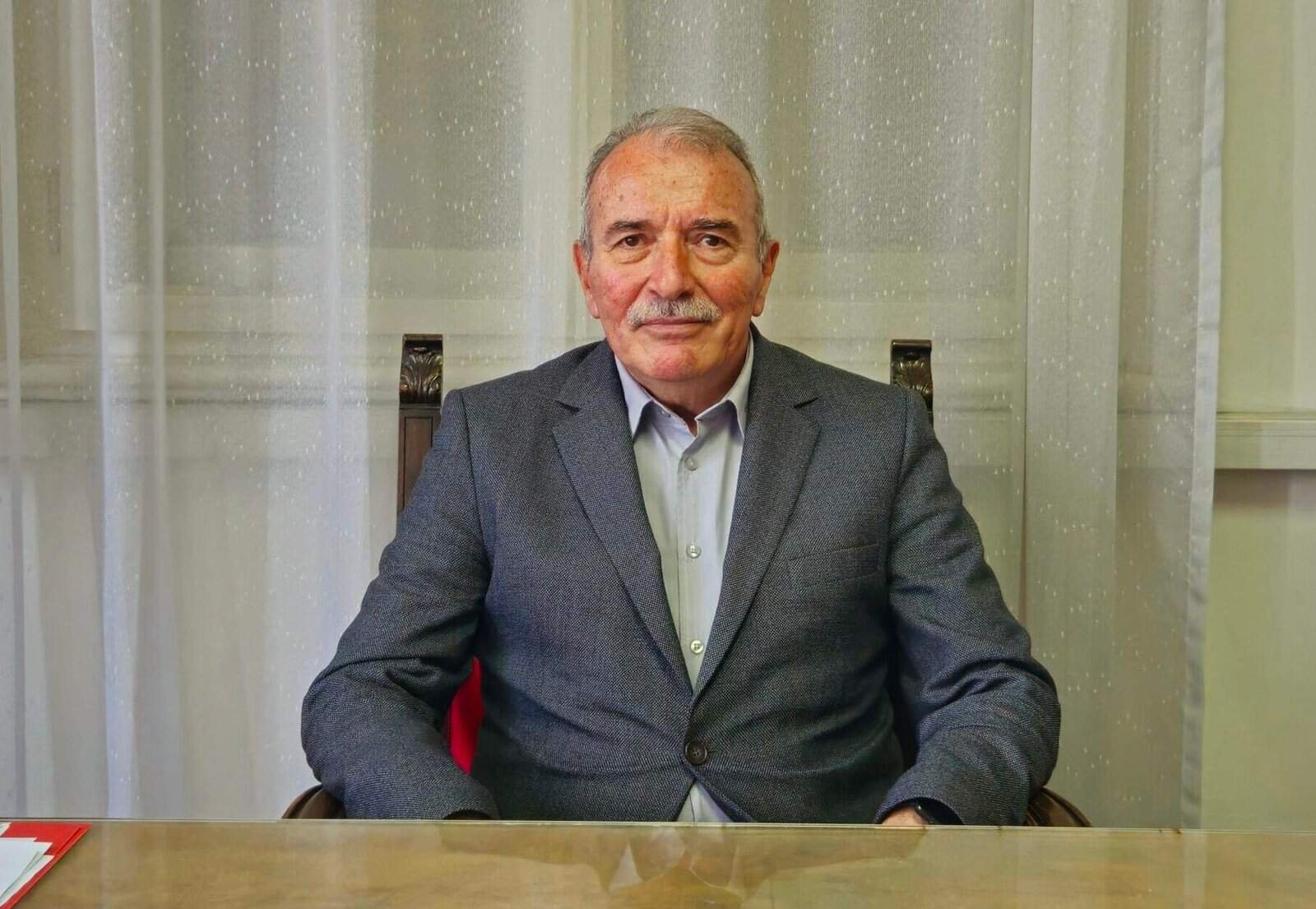 Muškarac u poslovnom odijelu sjedi za stolom, profesionalni izgled, unutarnji prostor.