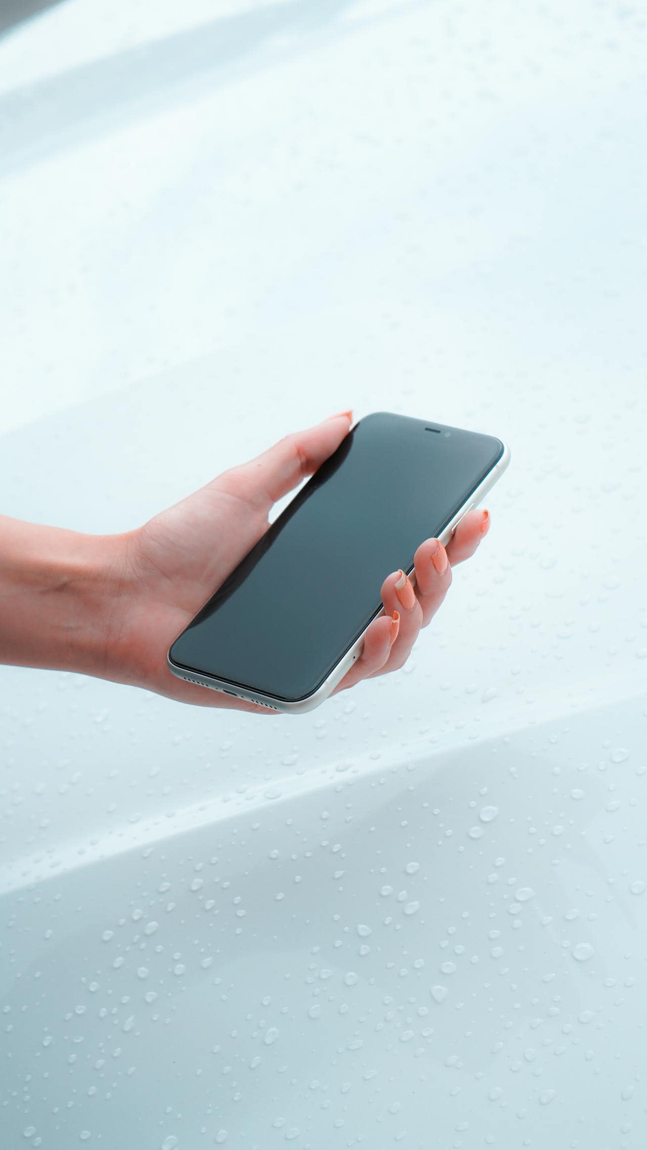 A person holds a black smartphone with a blank screen over a white, slightly wet surface dotted with water droplets. Suite Web Design Blog.