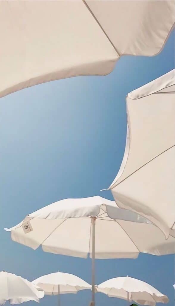 White beach umbrellas seen from below against a clear blue sky, creating a bright and summery atmosphere. Suite Web Design Page.