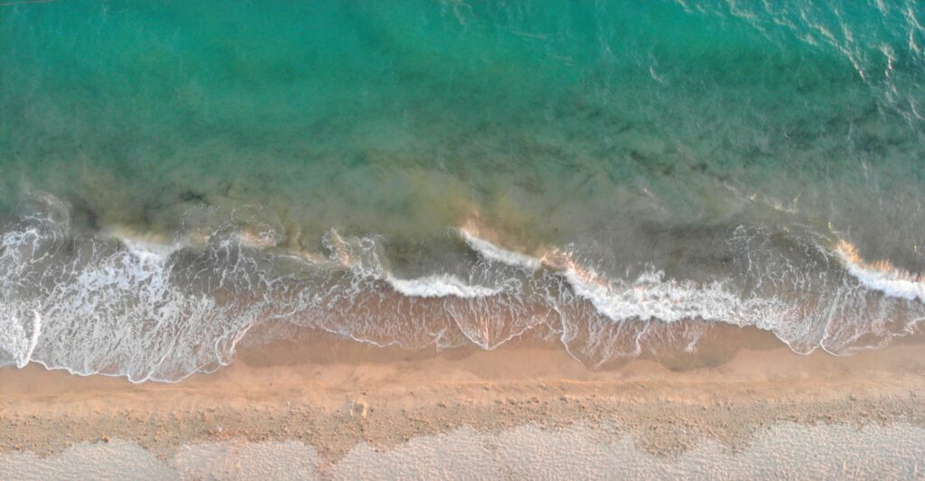 Aerial drone view of turquoise waves breaking on the sandy shore of Geremeas Beach, Sardinia.