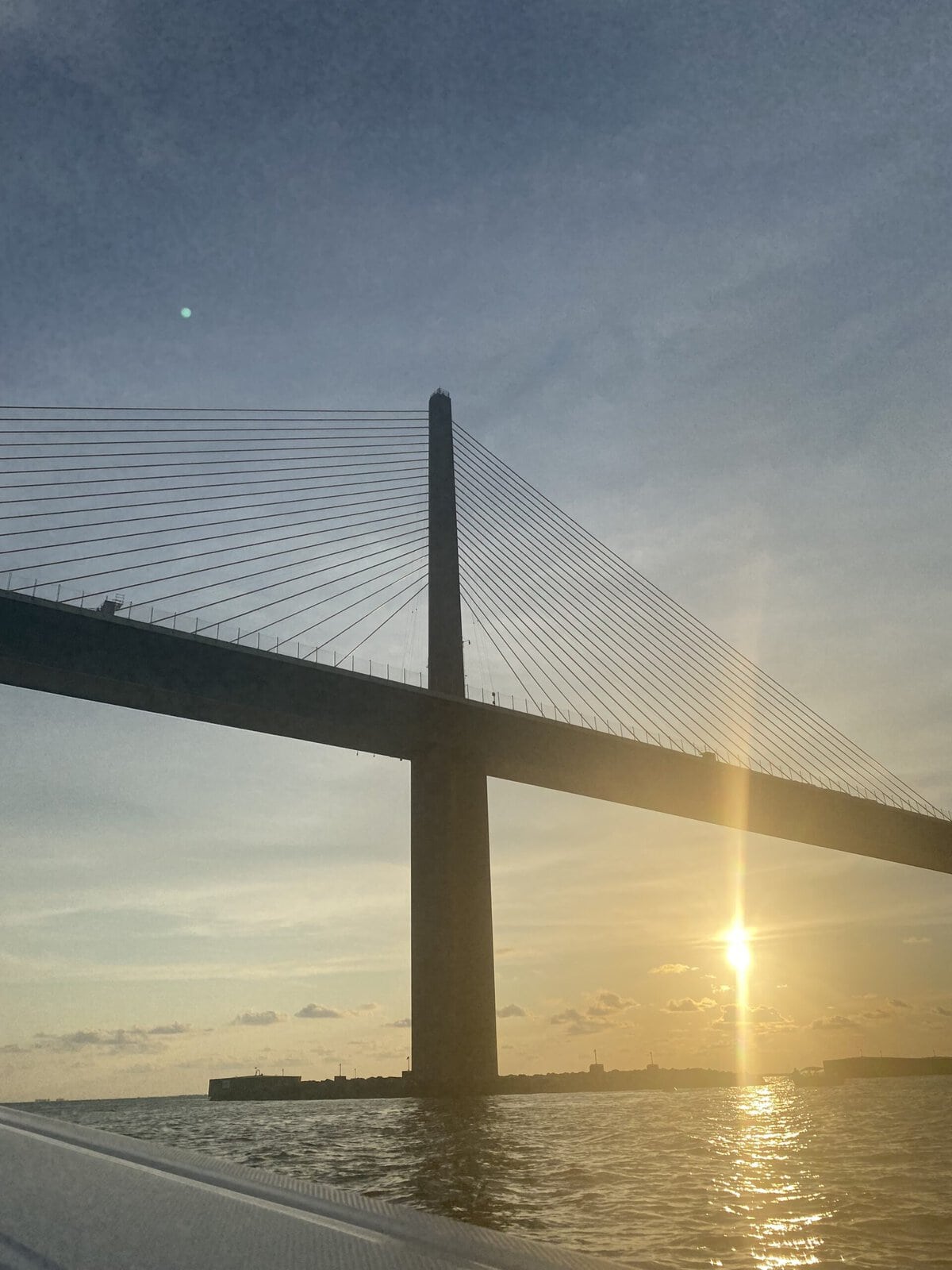 Sunshine Skyway Bridge silhouetted against a golden sunrise over Tampa Bay, viewed from a boat.