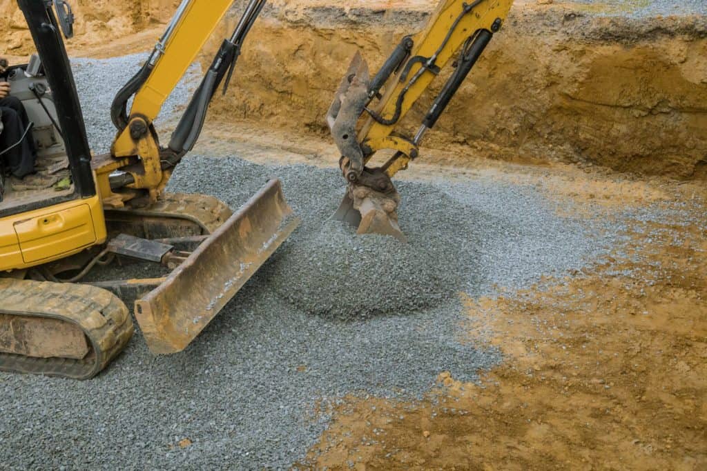 A yellow excavator from Superior Excavating spreads and levels gravel on a construction site, surrounded by dirt and partially excavated earth. Experience trusted service from one of the leading excavating companies in Michigan.