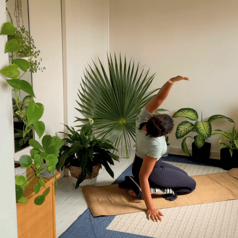 A black woman doing morning yoga during her morning yoga practice. She is surrounded by plants.
