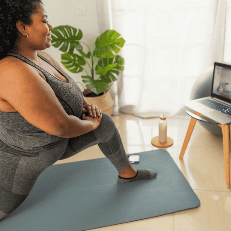 a woman doing yoga in house while watching a yoga class on her laptop and on her yoga mat