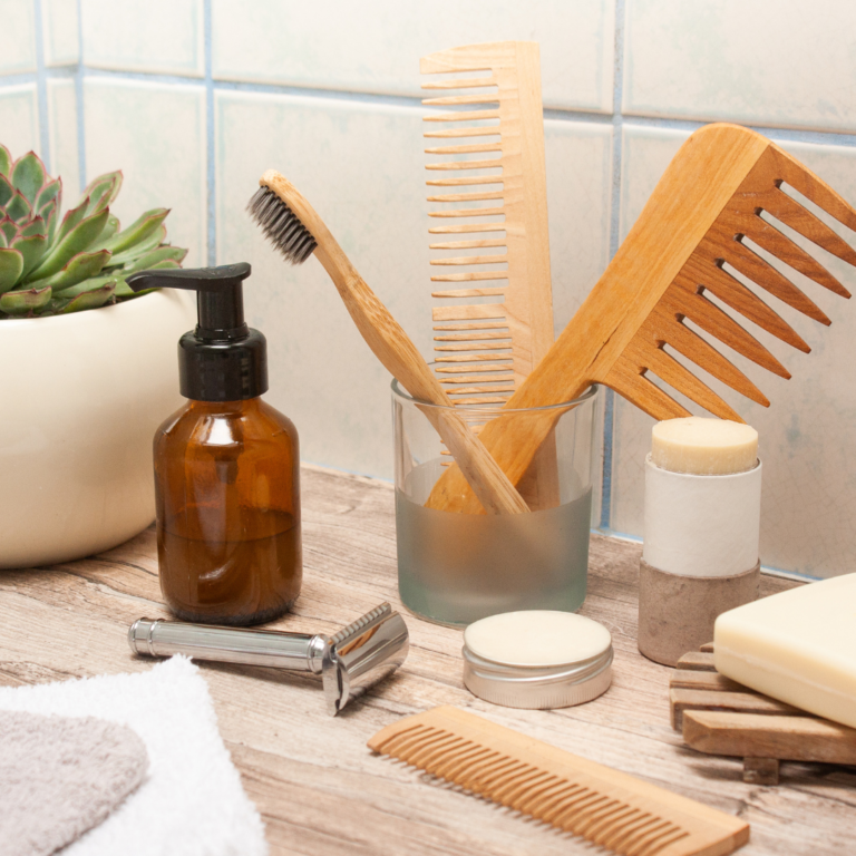 a zero waste bathroom with a bamboo toothbrush and comb, a stainless steel razor, a deodorant bar, and a zero waste skincare bottle.