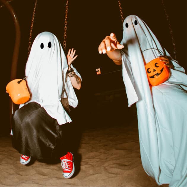 people dressed up as ghosts and holding Halloween decor at an outdoor Halloween party