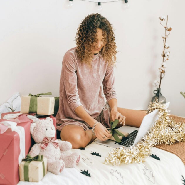 a woman wrapping a present and sending an e card for the holidays