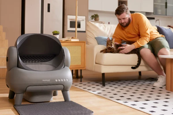 Man petting cat beside automated litter box