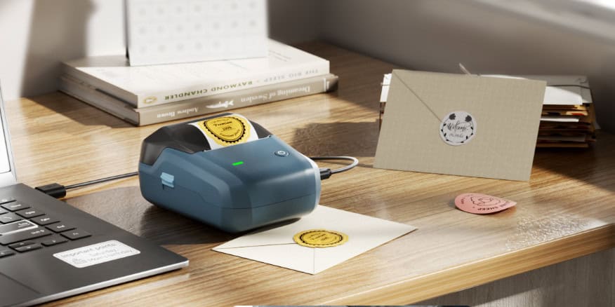 Label printer printing envelopes on wooden desk.