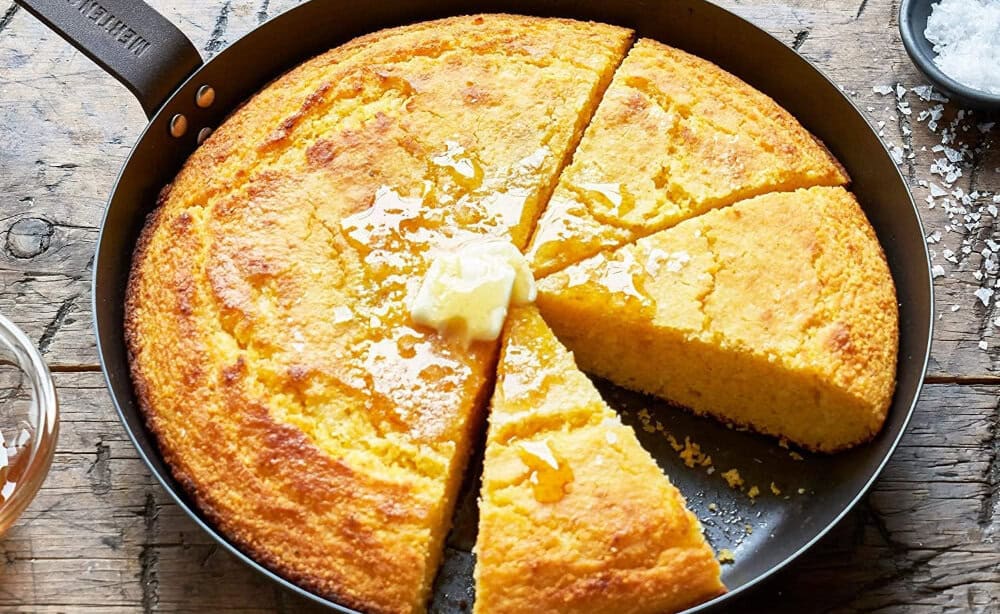 Sliced cornbread with butter and honey in skillet.
