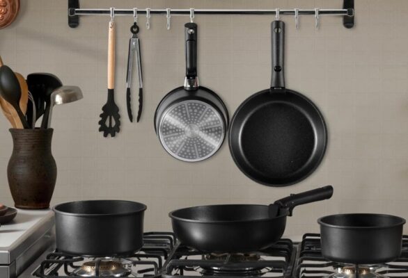 Black cookware set on kitchen stove and hanging rail.