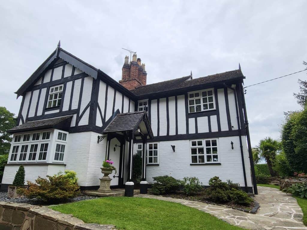 Historic Tudor-style home with black and white timber framing, landscaped garden, and decorative ext.