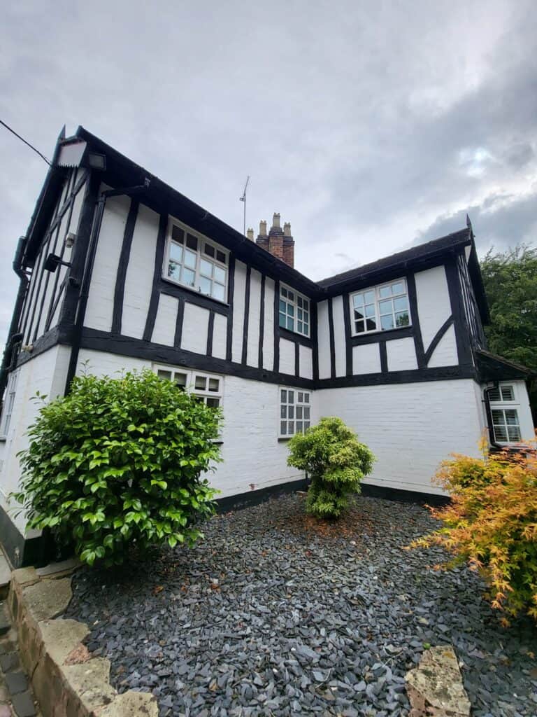 Historic Tudor-style house with black and white timber framing and lush garden.