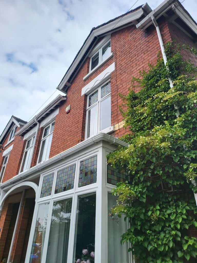 Victorian brick house with white window frames and lush greenery, painted by SWS Painters & Decorato.