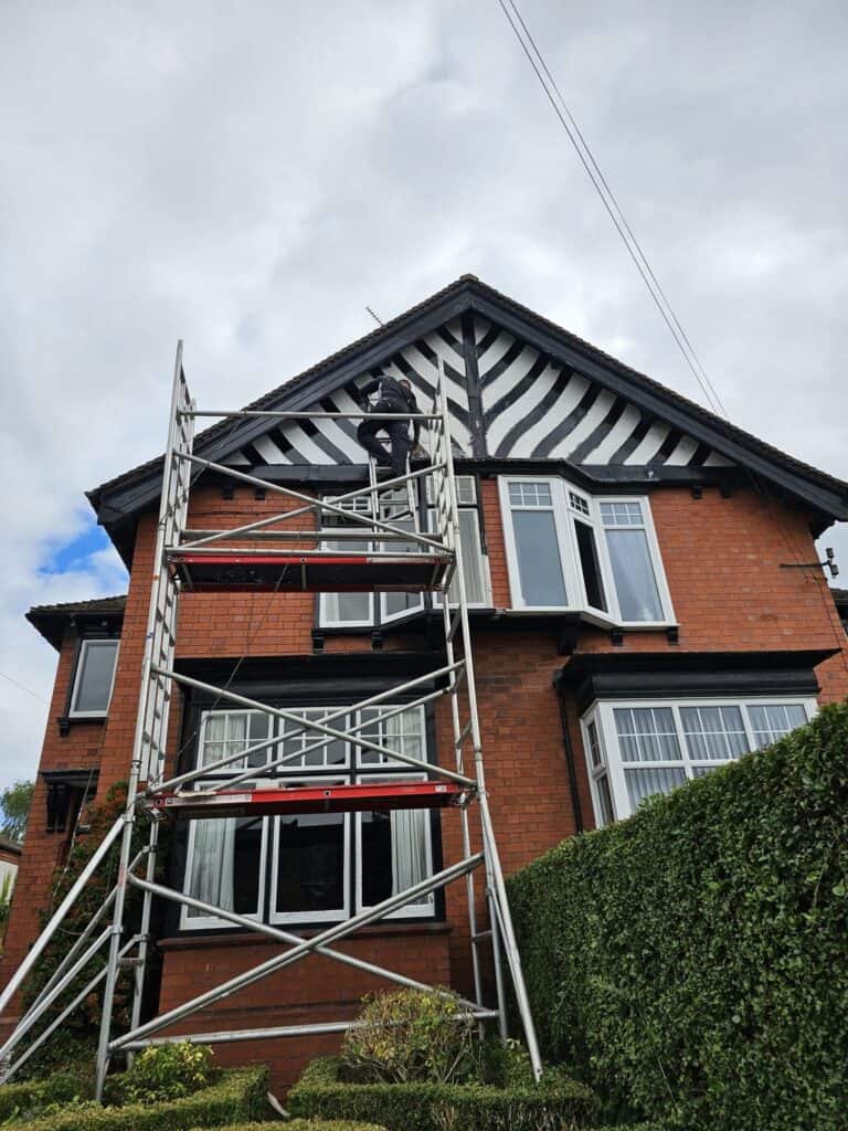 Exterior house painting in progress on a red brick home with scaffolding and decorative black and wh.