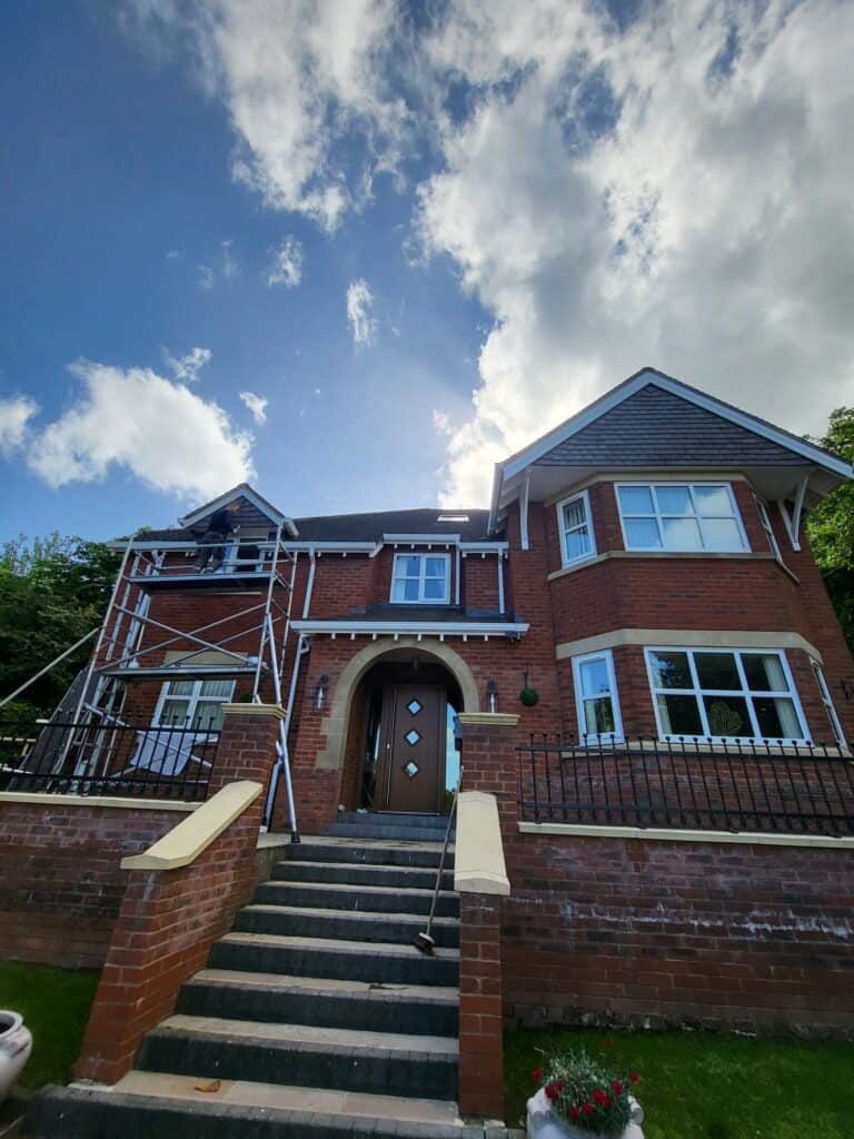 Classic brick home undergoing exterior painting or repairs, with scaffolding in place.