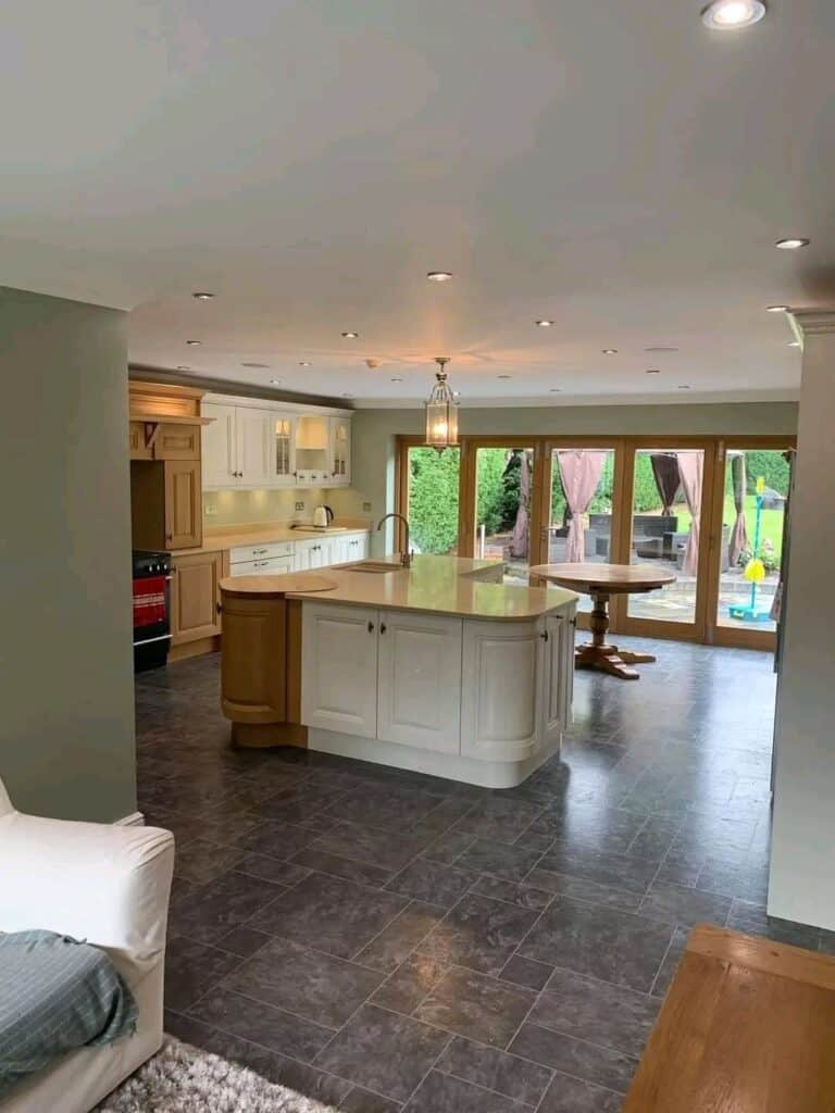Modern kitchen with wooden cabinets, island, and large glass doors to garden.