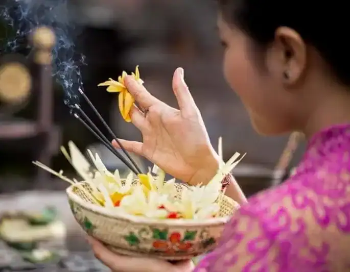 Femeie balineză efectuează ritual de purificare cu flori și bețișoare de tămâie.