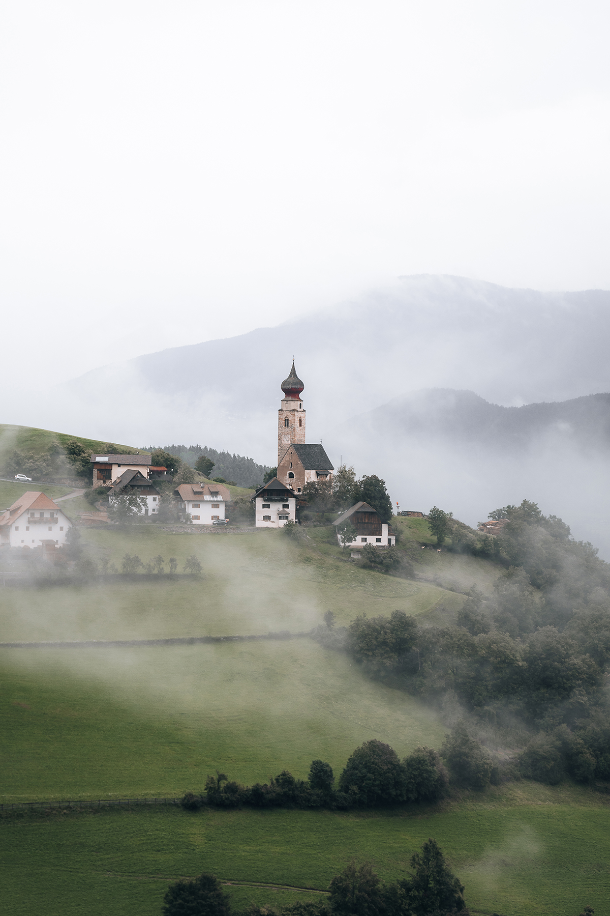Vilarejo enevoado na encosta de uma colina com uma igreja em degraus capturada com a lente Tamron 17-70 mm para paisagens em uma câmera sem espelho da Sony.