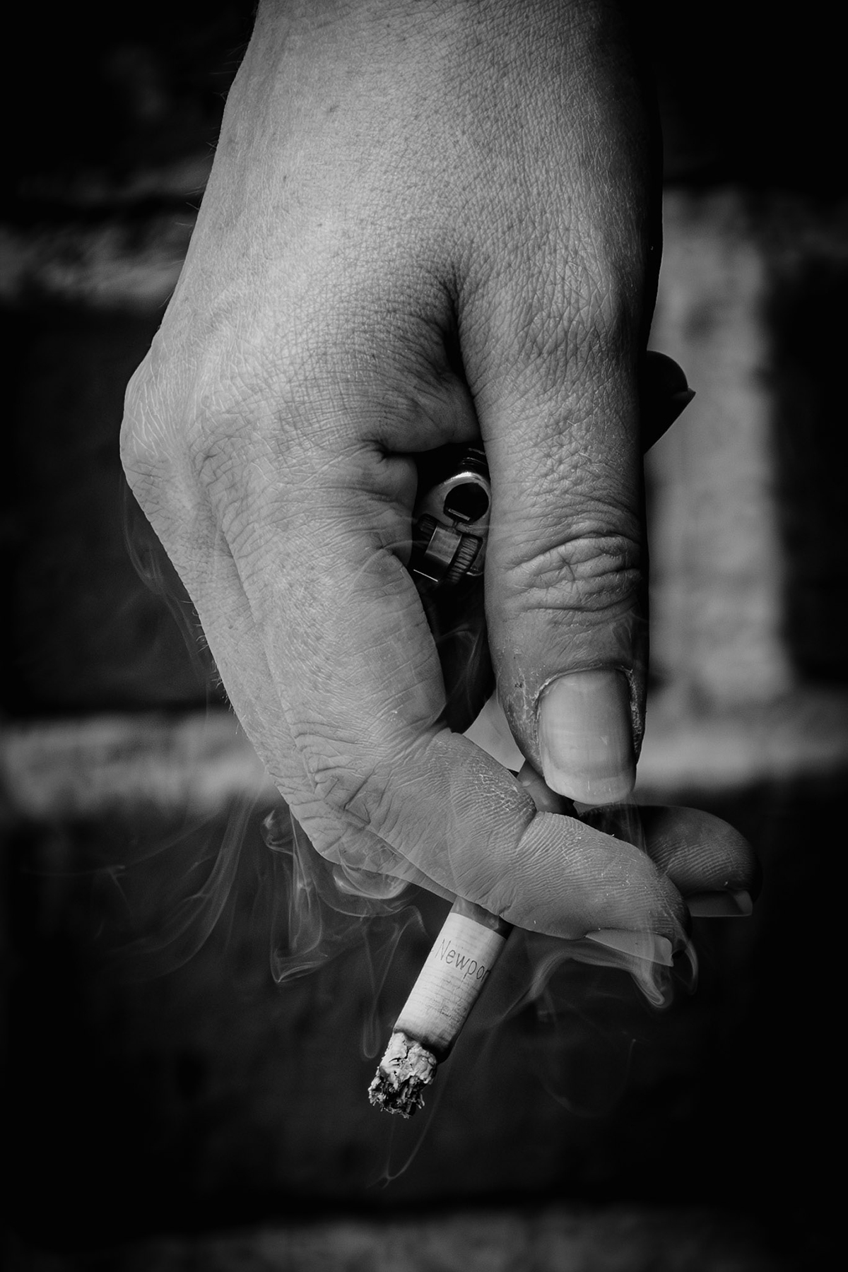 Photo monochrome de la main d'une personne tenant une cigarette allumée et un briquet.