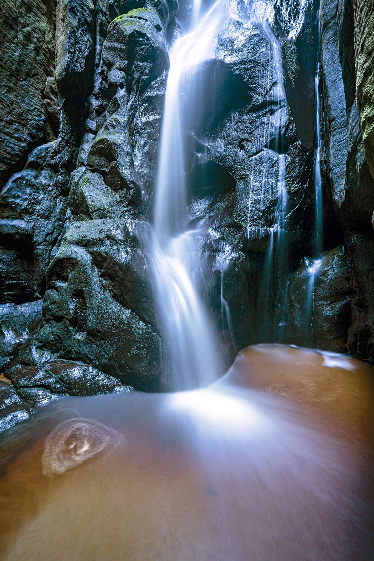 Larga exposición vertical de una cascada en un cañón rocoso, que ilustra la técnica de fotografiar agua en movimiento con un flujo suave y sedoso.