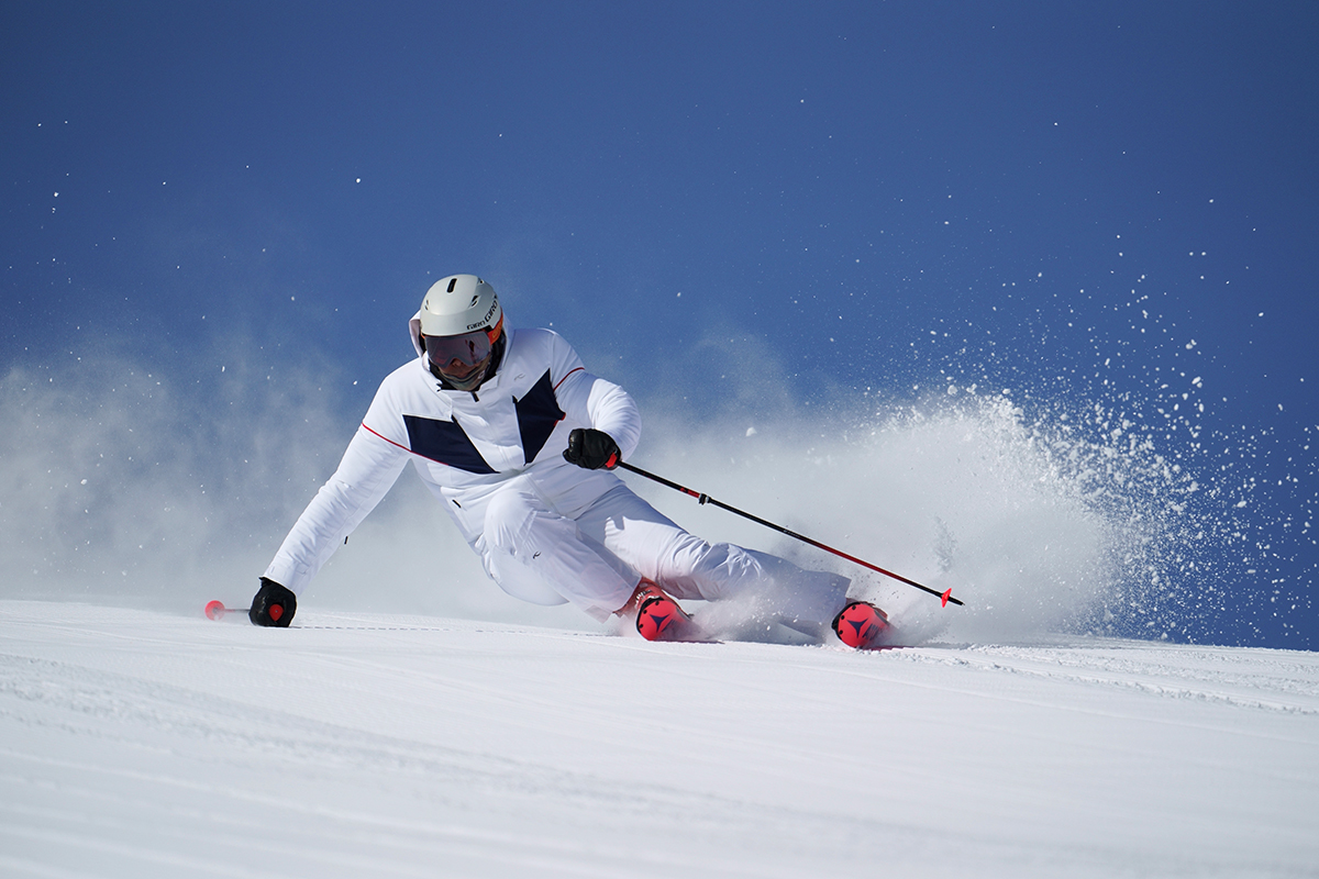 Winter sports photography capturing a skier in white gear carving through fresh powder on a bright, clear day.