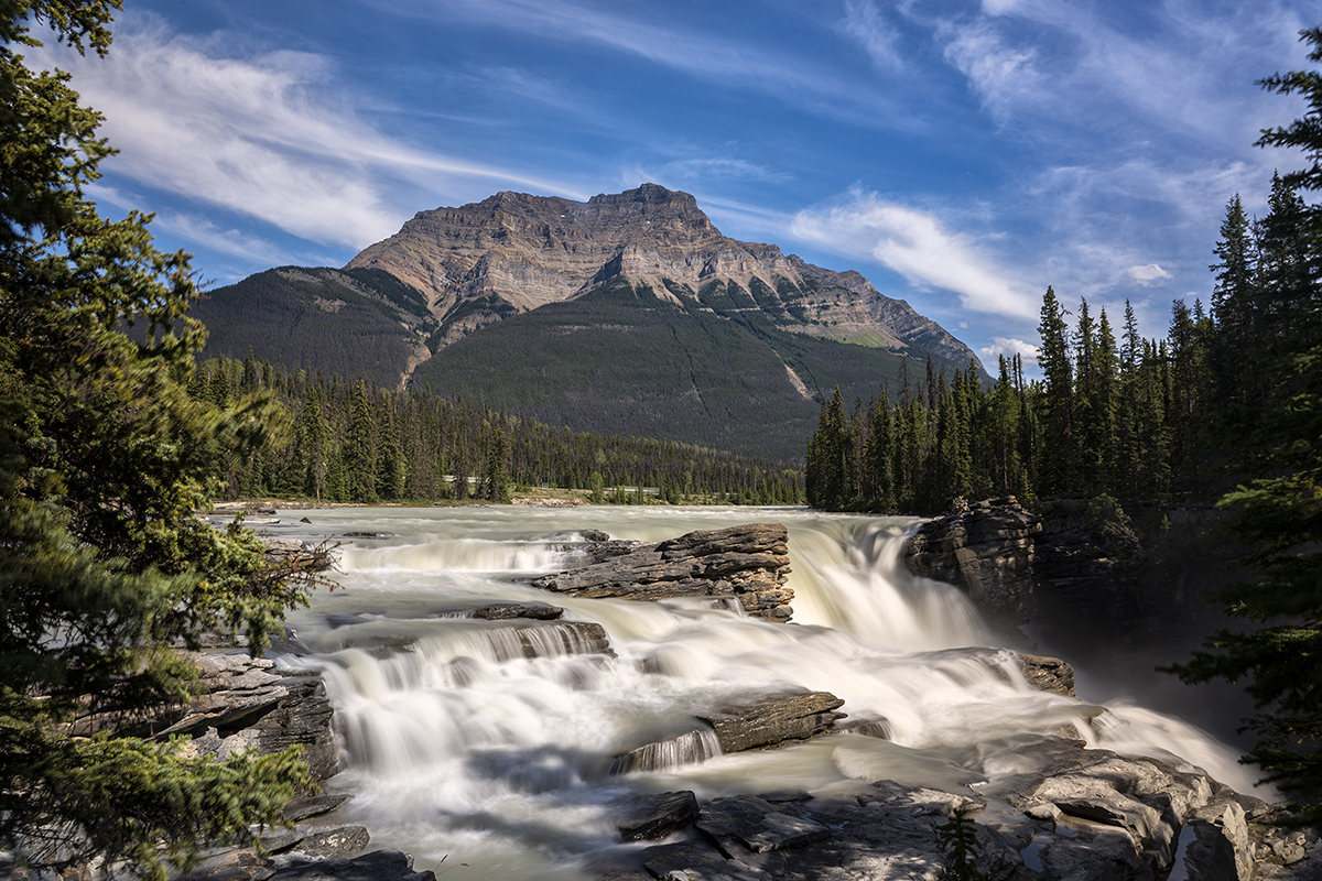 Paisaje de larga exposición que capta una cascada bajo una cadena montañosa, mostrando técnicas para fotografiar agua en movimiento en la naturaleza.