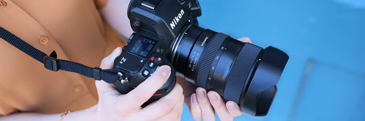 Mulher segurando uma câmera Nikon Z com uma lente Tamron 16-30 mm montada.