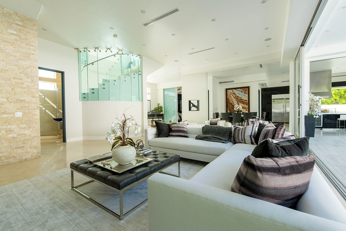 Sala de estar moderna e luxuosa com piso plano aberto e corrimão de vidro na escada, fotografada com lentes Tamron para fotografia arquitetônica de interiores.