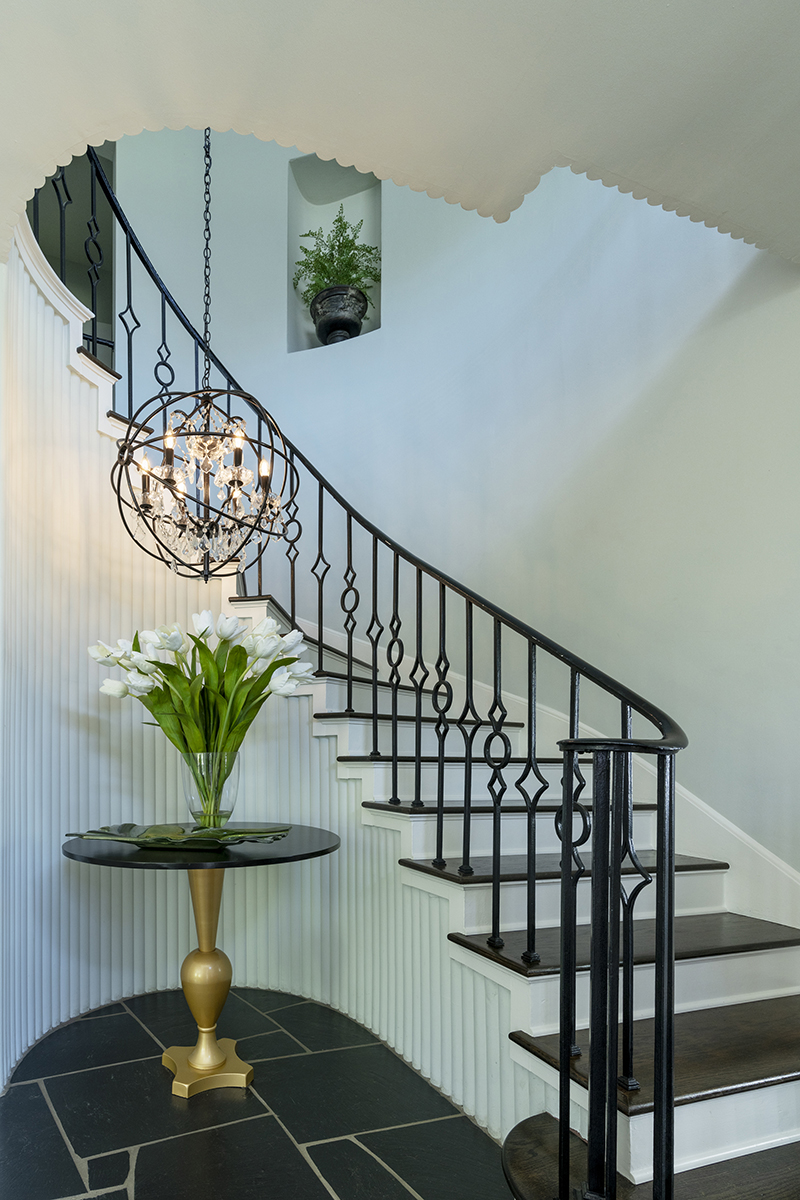 Escada curva elegante com corrimão de ferro preto e lustre, capturada usando lentes Tamron para fotografia arquitetônica de interiores de luxo.