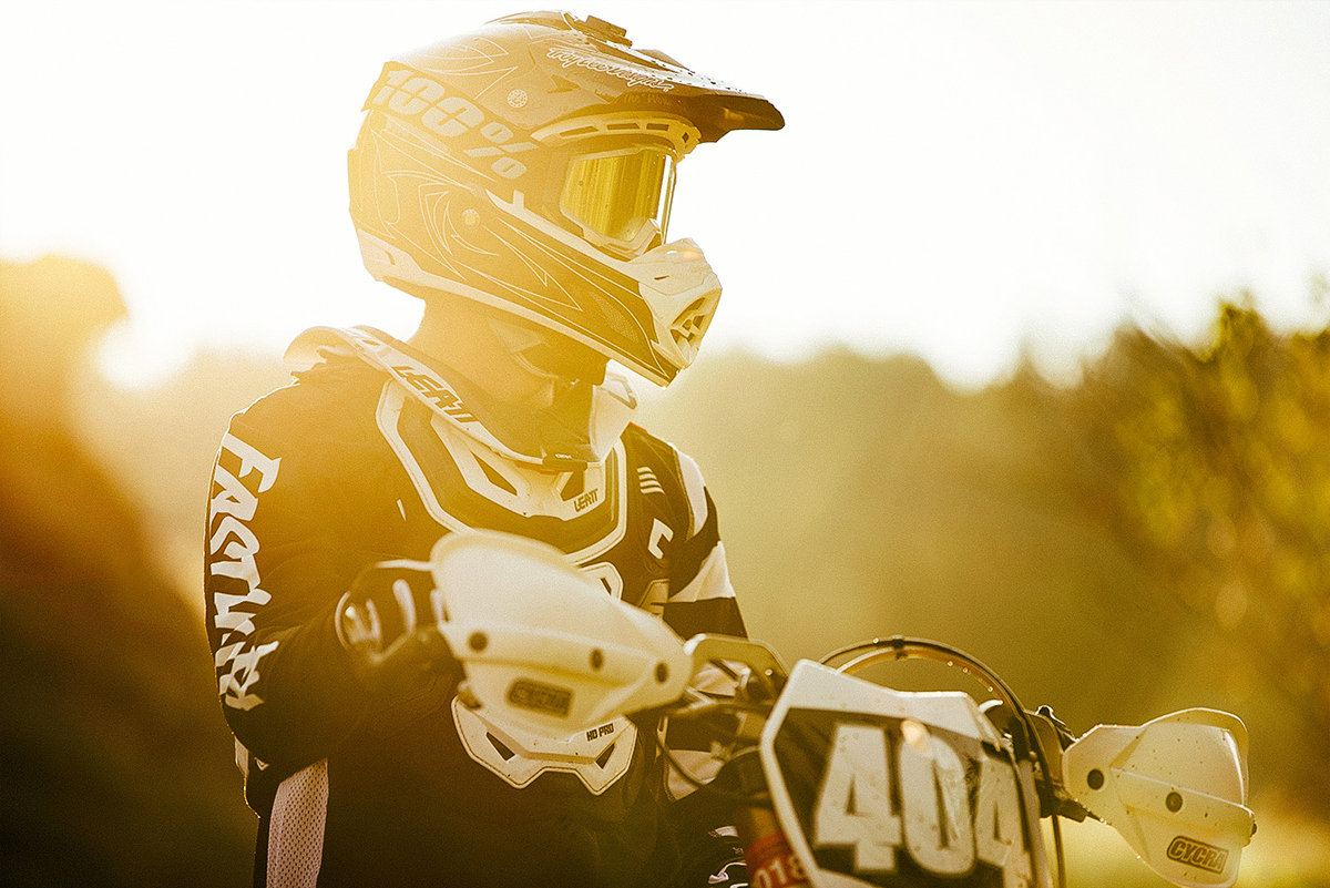 Gros plan d'un pilote de motocross avec son casque et son équipement à l'heure dorée, illustrant les conseils d'éclairage pour la photographie de moto et les techniques de portrait de pilote.